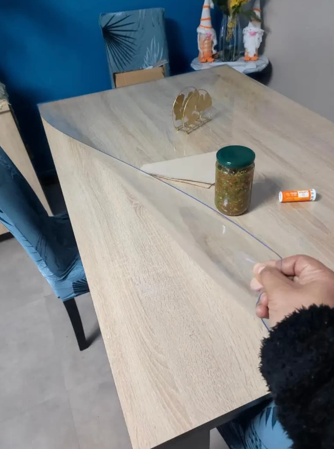 Una mano levanta un rincón de la estera transparente de la mesa de luz; junto a un frasco de conservas