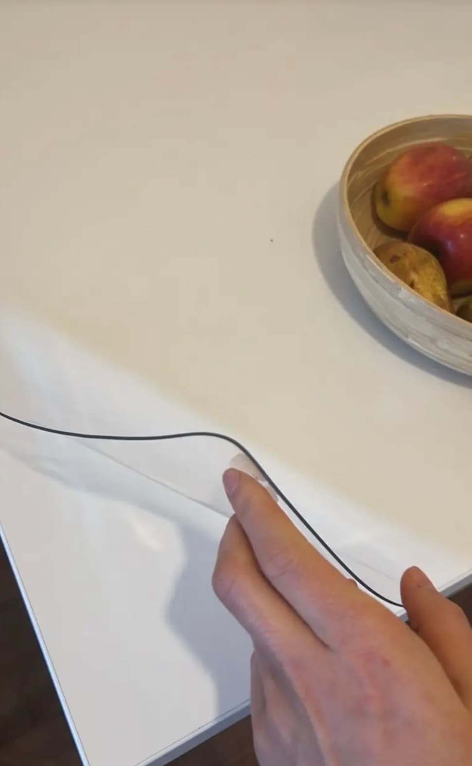Top blanco con un tazón de manzanas y peras; una mano lisa el borde de la alfombra transparente
