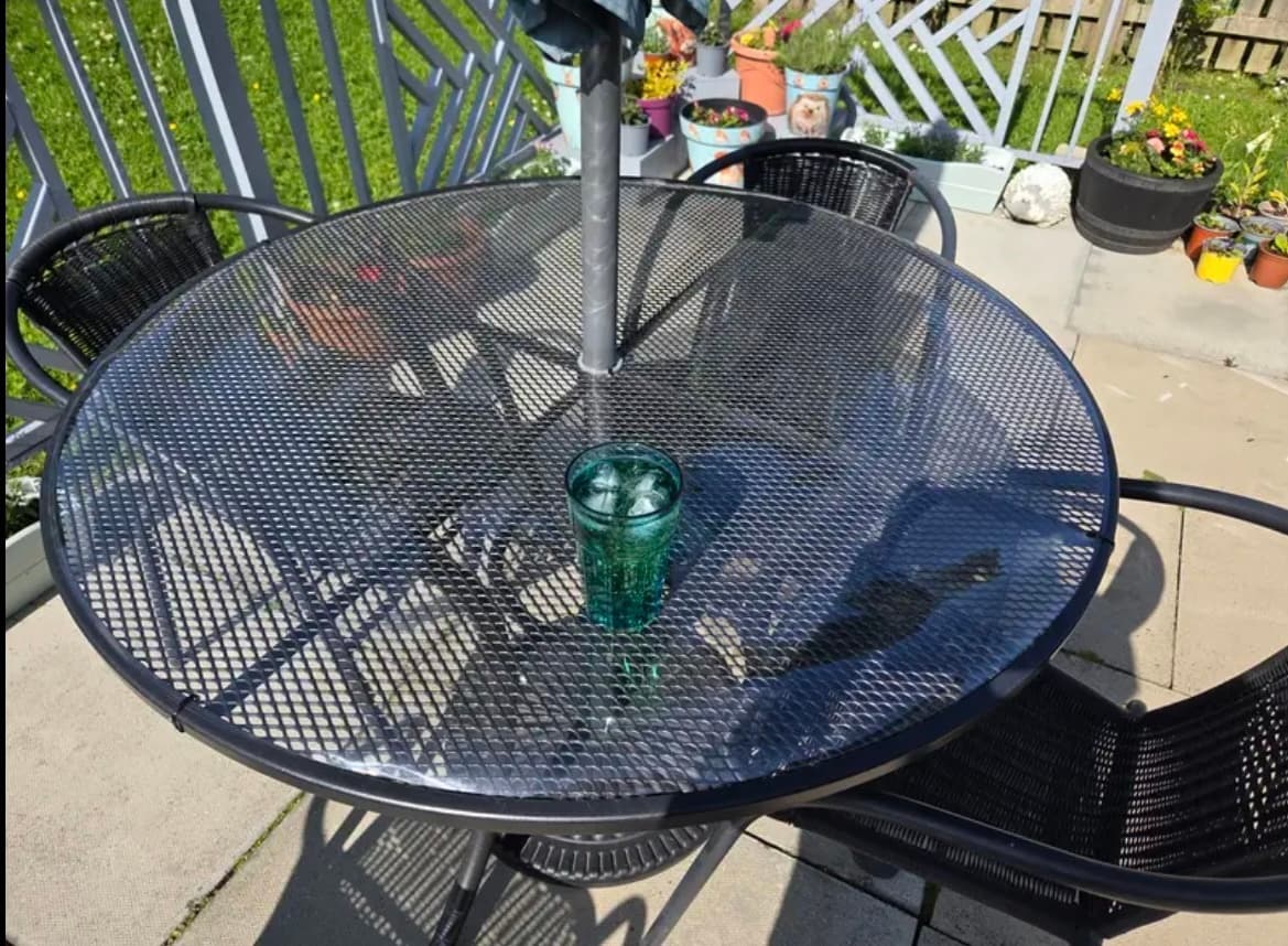 Alfombra sobre la mesa redonda en la terraza, un vaso en el centro y macetas de flores alrededor