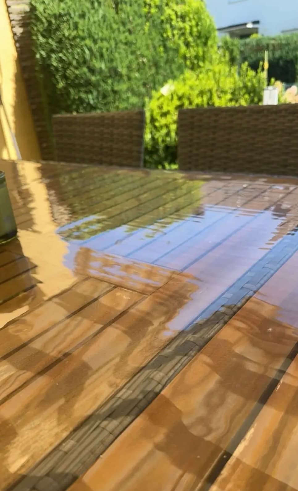 Mesa de jardín en listones de madera: en el vidrio suave se refleja la cobertura y el cielo