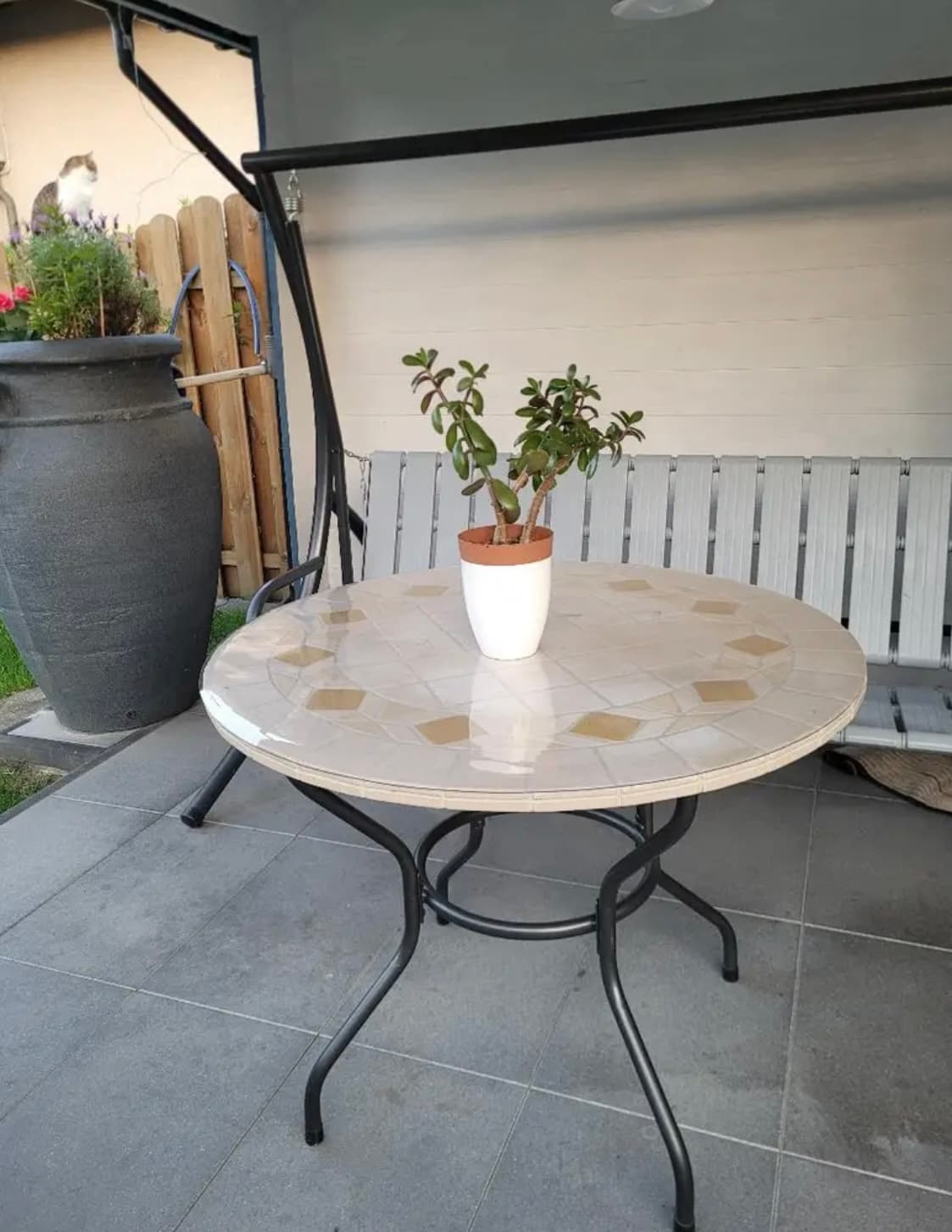 Mesa redonda con mosaico superior en la terraza, una planta audaz descansando en la estera
