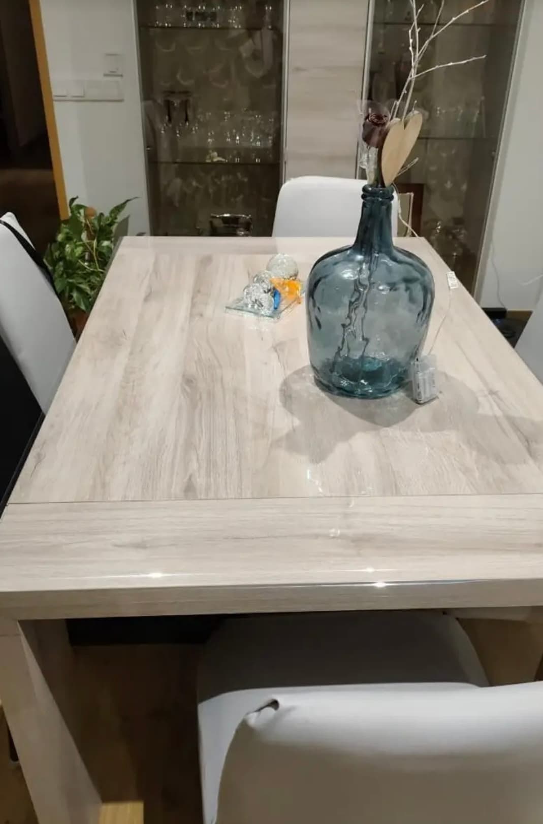 Mesa ampliable en madera ligera con una gran damigiana azul sobre vidrio suave