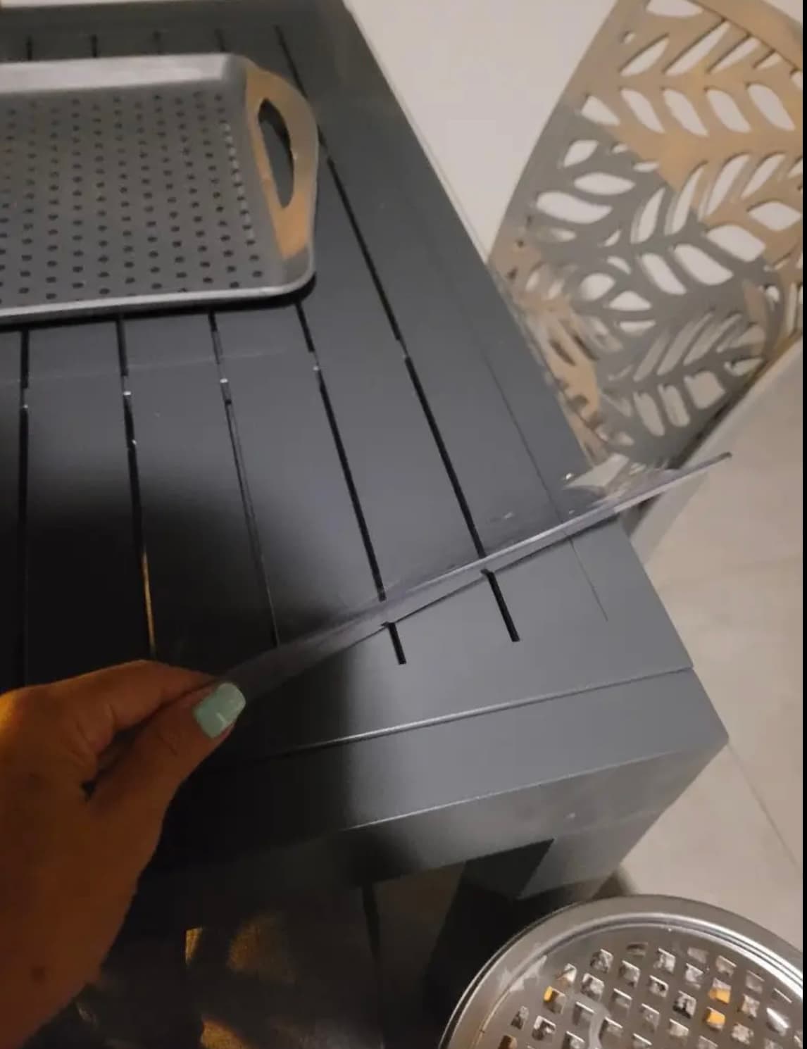Una mano levanta la esquina de la colchoneta de una mesa antracita a las lamas, junto a las bandejas metálicas