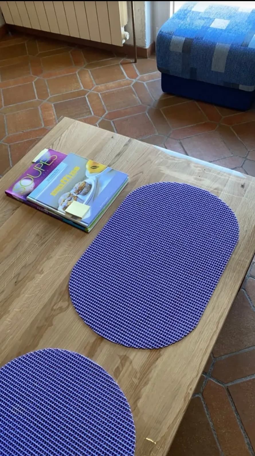 Mesa de roble con manteles púrpuras y libros de cocina; el borde de la estera protruye del suelo