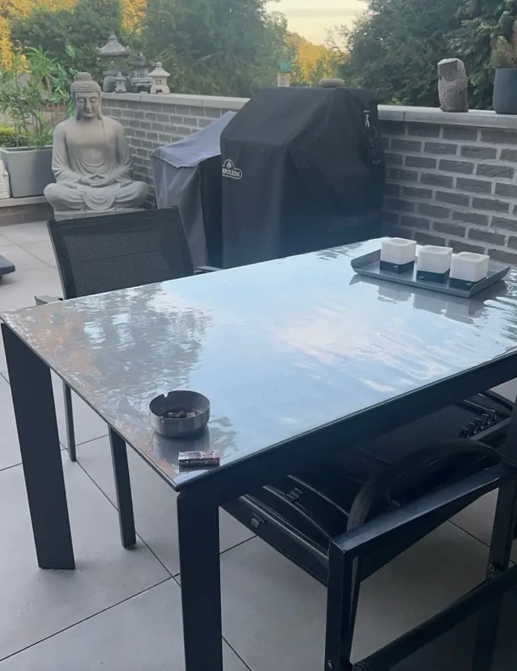 Terraza con barbacoa y estatua de piedra: mesa de marco negro cubierta por alfombra transparente