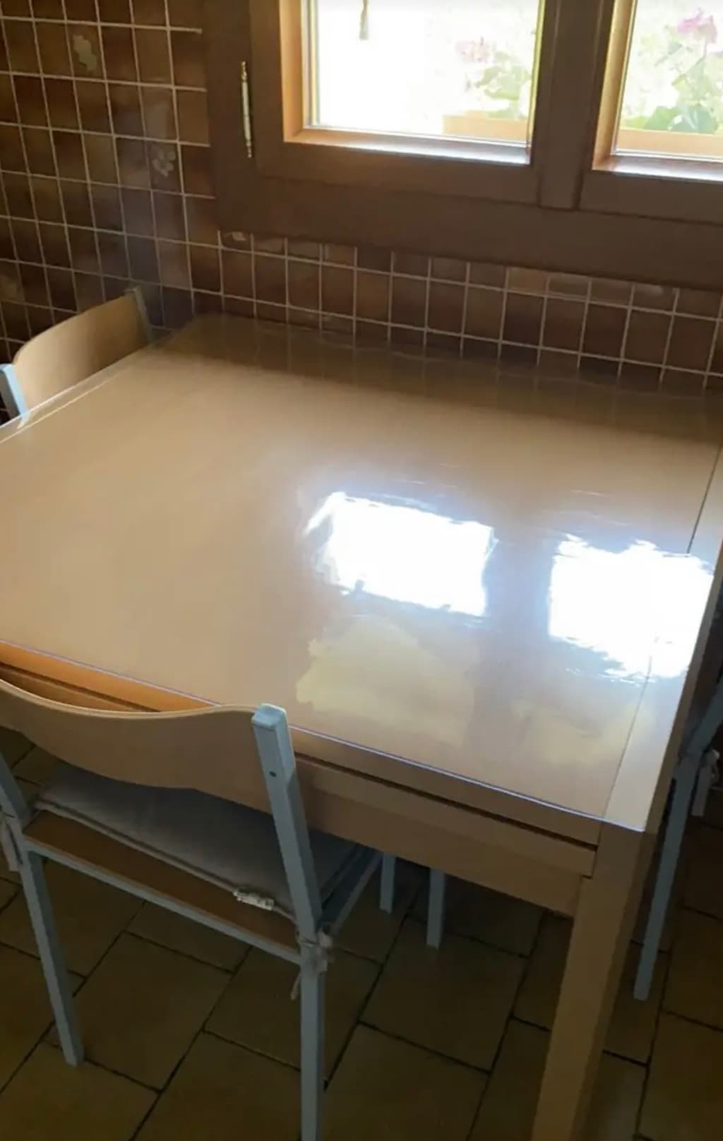 Paño de mesa pequeño en una cocina de azulejos: en el suelo la estera, geranios en la ventana