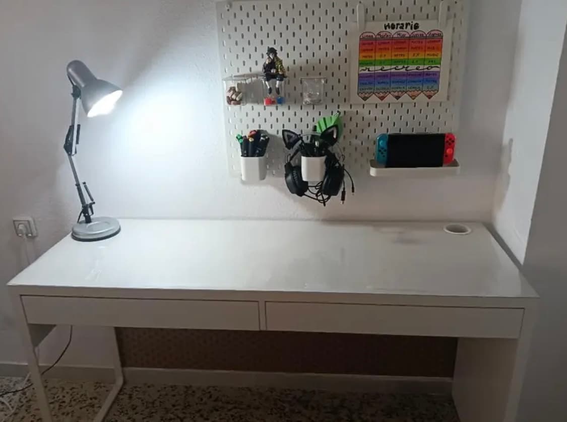 Escritorio blanco con lámpara y panel perforado a la pared; el plan y protegido por la película