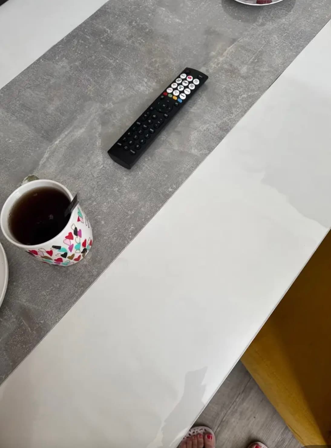 Mesa blanca con banda de hormigón gris: taza de té y control remoto descansando en la estera