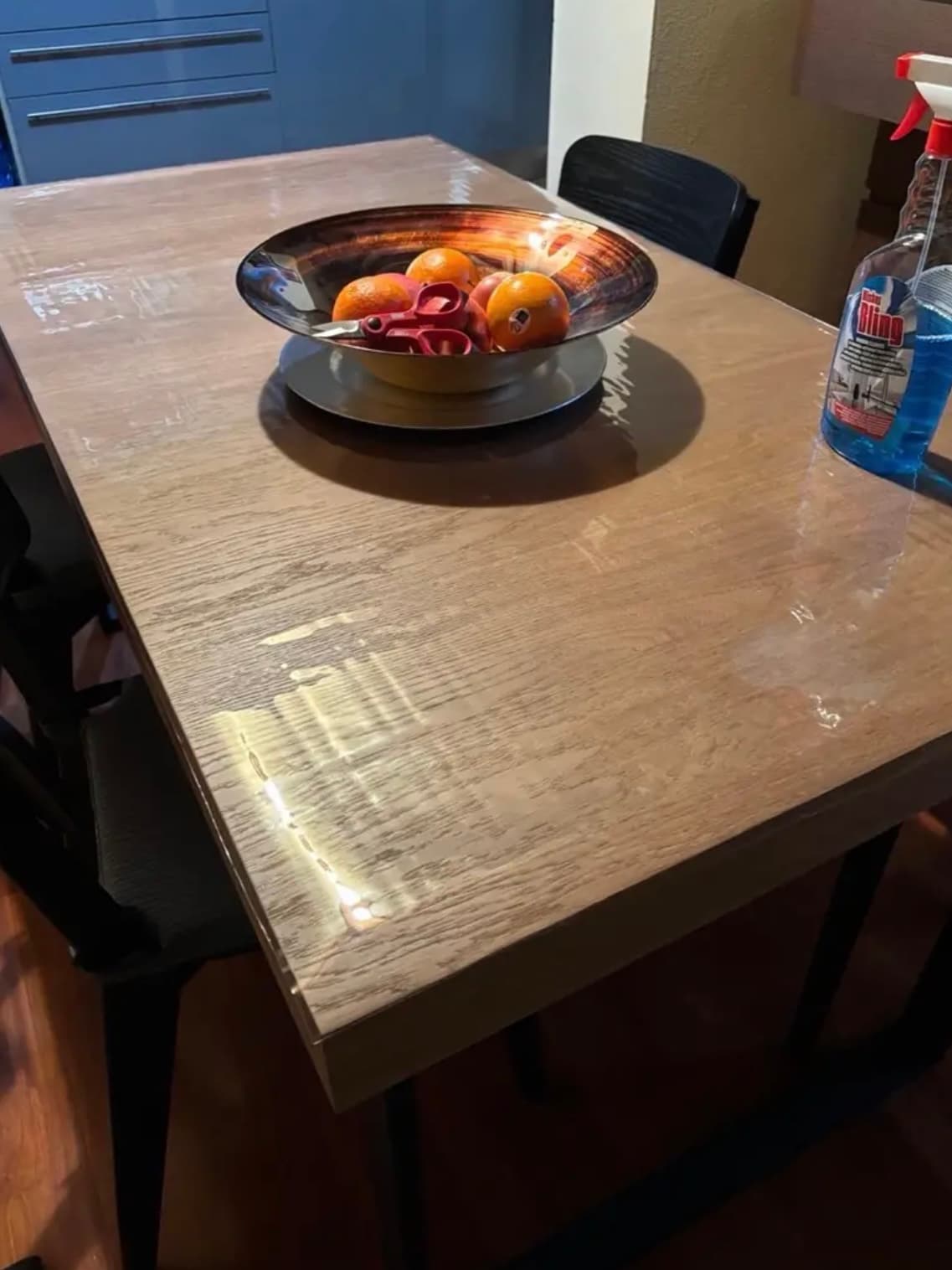 Tazón de metal con naranjas en el suelo de roble; junto a la estera una botella de detergente