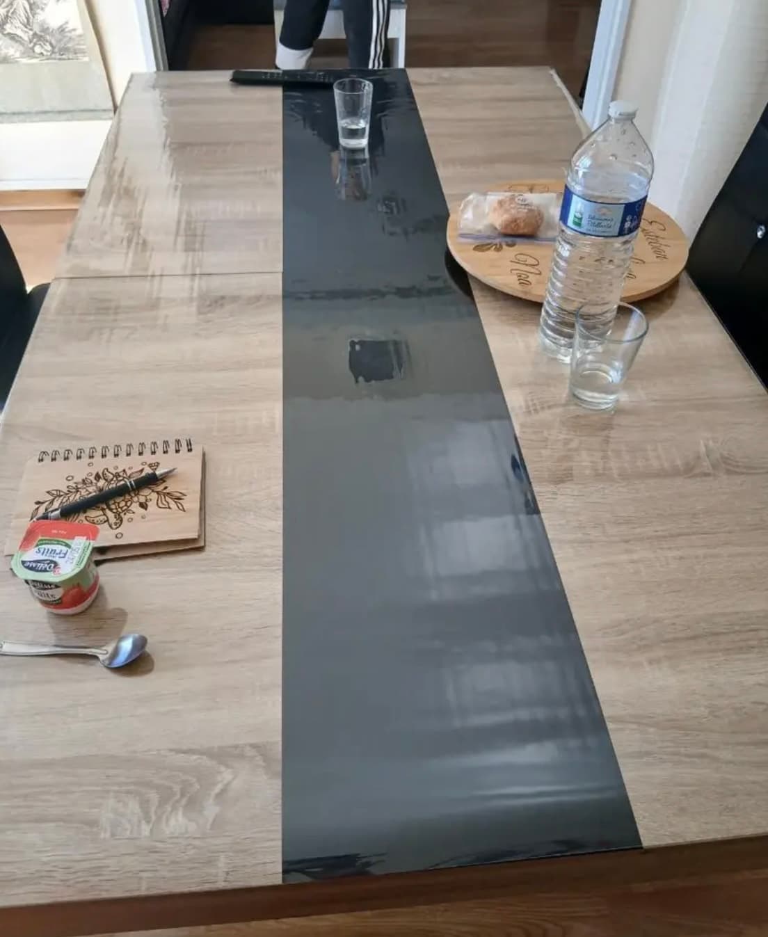 Desayuno en una larga mesa con banda gris: agua, vasos y cuaderno sobre la alfombra