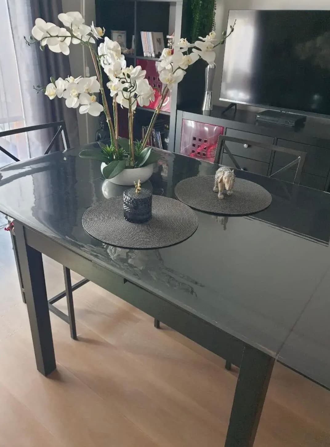 Mesa antracita en salón con orquídeas blancas y manteles redondos, piso debajo de la estera